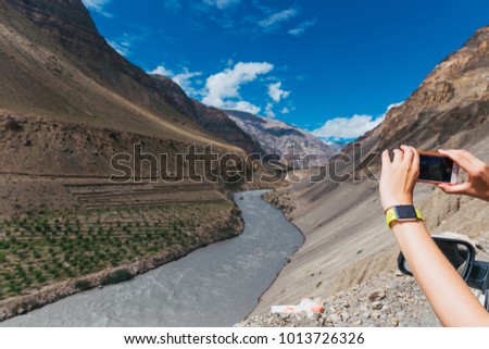 July 2017 - Himachal Pradesh, India - view at Spiti river valley from side window of a moving car. Taking a picture with a smartphone with a smartwatch on wrist.