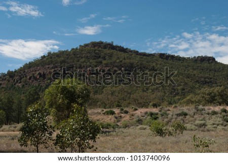 a big hill in a rural paddock with clouds in the sky on a sunny day