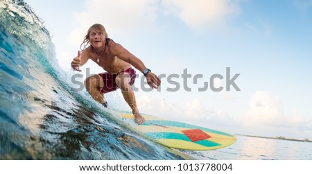Young surfer rides ocean wave and shows the Shaka sign. Extreme sport and active lifestyle concept Royalty-Free Stock Photo #1013778004