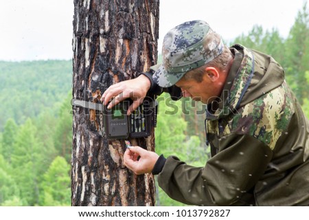 Foresters install cameras of a photo-trap with infrared radiation and a motion detector, attached by straps on a tree, photograph animals and wildlife in the Siberian taiga.