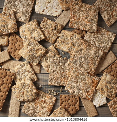 Various crispy wheat, rye and corn flatbread crackers with sesame and sunflower seeds on rustic grey wooden background. Top view point.