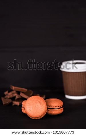 Chocolate macaroons and a paper cup with coffee on a dark background. A gift, a surprise for Valentine's Day, a woman's day, a mother's day.