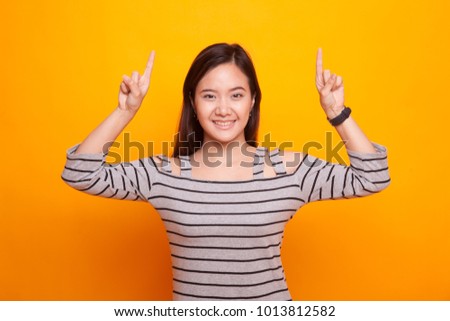 Young Asian woman point to blank space on yellow background