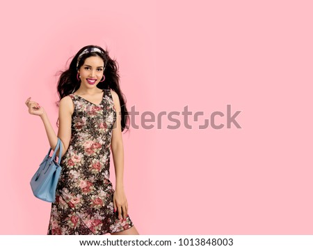Cheerful Beautiful Young Woman in a Pretty Mini Dress with Pink Flowers With Holding Blue Turquoise or Blue Ocean Handbag Posing over Pink Background. Fashion Spring Summer Photo with Copy Space