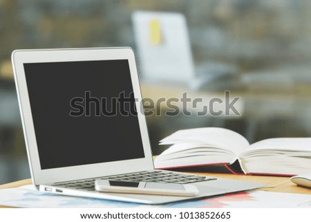 Close up of modern table with empty white laptop, supplies and other items on blurry city view background. Mock up 