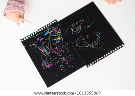 Close up of baby hands drawing on magic scratch painting paper with drawing stick.