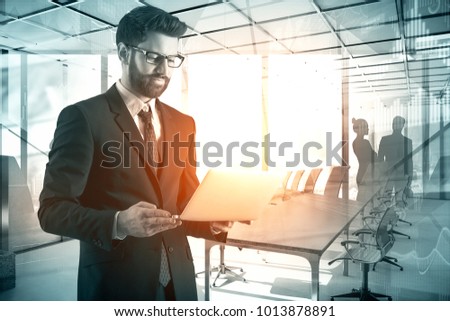 Businessman using laptop on abstract office interior background with sunlight. Technology and meeting concept. Double exposure 