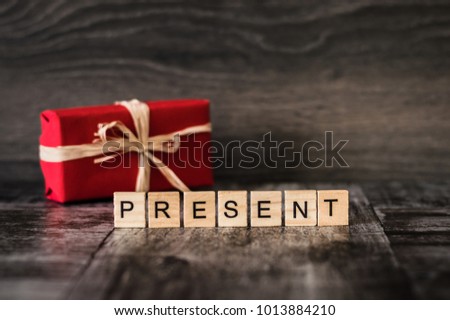 the word "present" is made of bright wood cubes with black letters of the English alphabet and a gift in red box on dark wooden background
