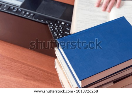 Books and laptop on the desktop. The hand lies on the book