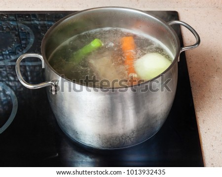 cooking soup - simmering meat stock in stockpot on ceramic cooker