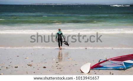 Picture of a girl in a wetsuit walking into the sea after an intense windsurfsession
