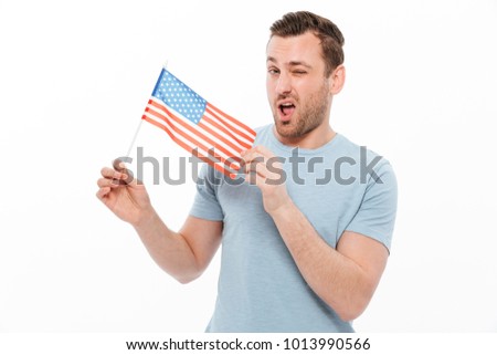 Photo of attractive man having bristle positively demonstrating small american flag and winking on camera isolated over white background