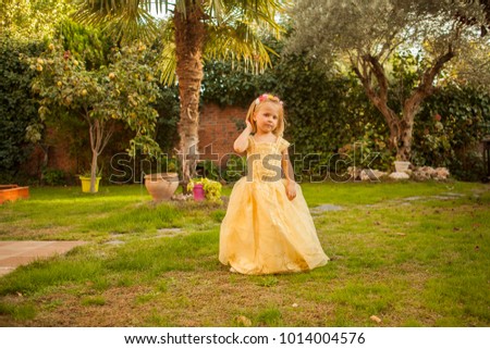 Baby girl in a princess costume playing in the garden. Outdoors.