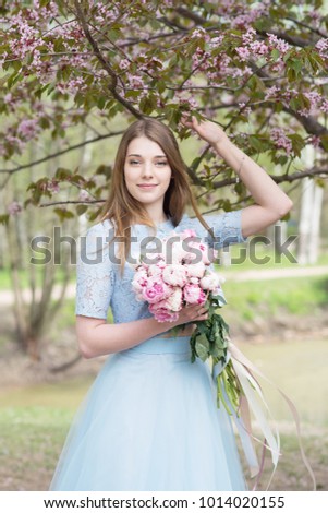 Slavic girl in spring in park. sakura blossom background with bouquet of peonies.