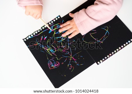 Close up of baby hands drawing on magic scratch painting paper with drawing stick.