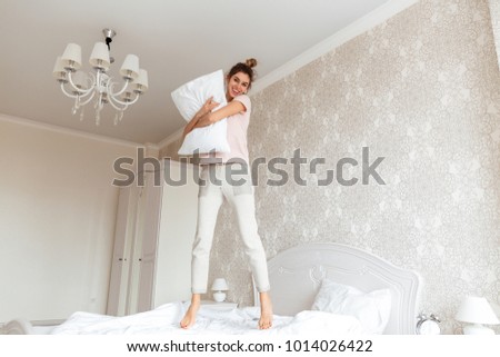 Full length image of Happy young woman having fun on bed with cushion at home