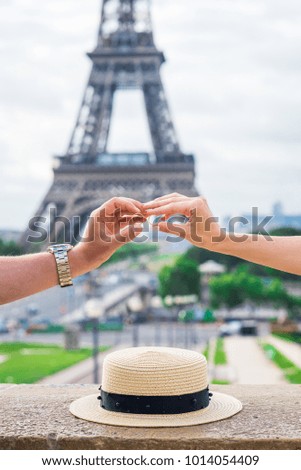 Man and woman hands holding wedding rings close to each other. Eiffel tower view background