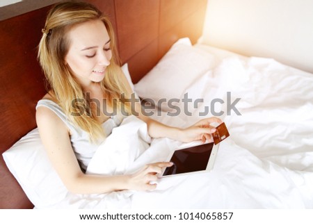 woman paying money for travel holds debit credit card and tablet in white bed at home. concept of new technologies, online shopping buy goods with sunshine
