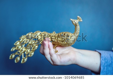 golden toy bird sitting on a hand on a blue background close-up