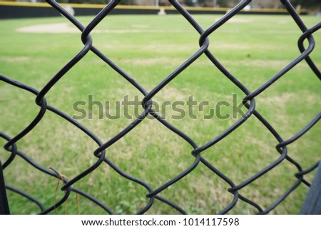 A view of an empty outdoor green field through the metal chain links on a sunny day.