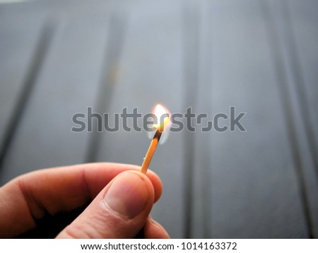 Lit match held in hand on black rugged background.
