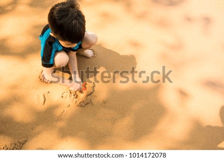 A boy in swimming suit is sitting on the beach and playing sand at the sea in the sunny day in summer.