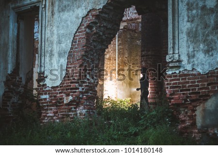 A hole in the wall of an ancient cathedral. The girl is shining with a lantern. Silhouette of a girl in an abandoned church. Ruins of the church.