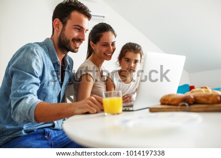 Family breakfast.Young parents with they daughter sitting at the table and watching cartoons on laptop.