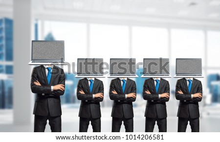Businessmen in suits with laptops instead of their heads keeping arms crossed while standing in a row inside office building.