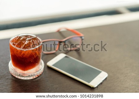 Ice water in glass. Placed beside a white mobile phone. The glasses are placed side by side on a wooden table.