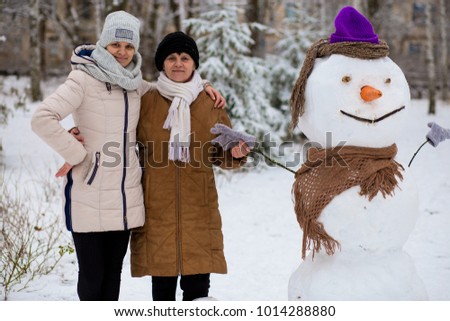 Mother and adult daughter sculpt a big real snowman, Happy family in winter park