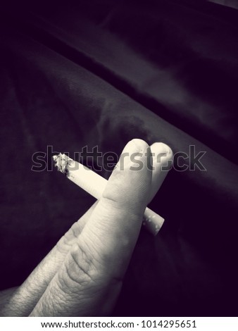 Male fingers holding a cigarette on dark background. Vertical black and white picture. Smoking concept