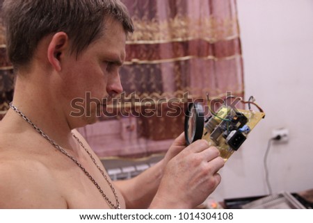 Pictured in the photo a young man who looks in a magnifying glass on a microcircuit.
