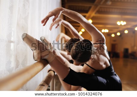 three young cute ballerinas perform exercises on a choreographic machine or barre on the background of a ballet class Royalty-Free Stock Photo #1014324076