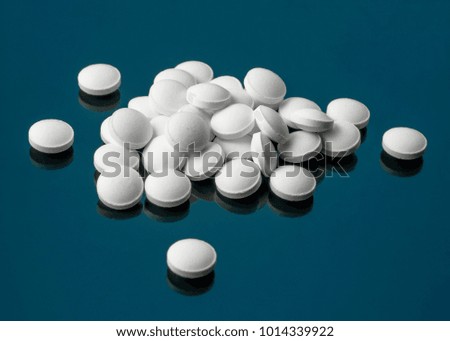 Round white tablets scattered on a blue, green background.