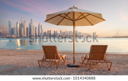 Beautiful beach in Dubai with 2 sun chairs and an umbrella. In the background is the skyline of Dubai Marina Royalty-Free Stock Photo #1014340888