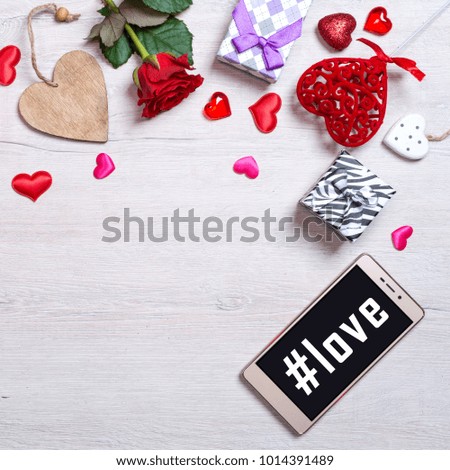 Love background with hearts, gifts, red rose and smartphone. Hashtag love on the smartphone screen