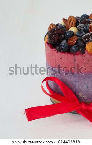 Raw cashew cake in form with pecans, macadamia, blueberries, blackberries on white background