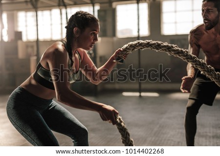 Strong woman exercising with battle ropes at the gym with male trainer. Athlete doing battle rope workout at gym with instructor. Royalty-Free Stock Photo #1014402268