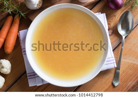 Bone broth made from chicken on a wooden table, with vegetables in the background, top view