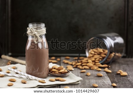 Organic chocolate  almond milk in a glass bottle with whole almonds spilled over a rustic wooden table. . Focus on nutmilk with blurred background.