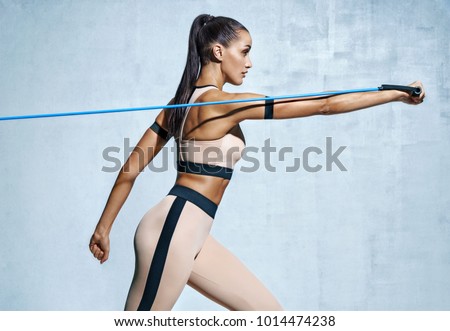 Strong woman using resistance band in her exercise routine. Photo of fitness model workout on grey background. Strength and motivation