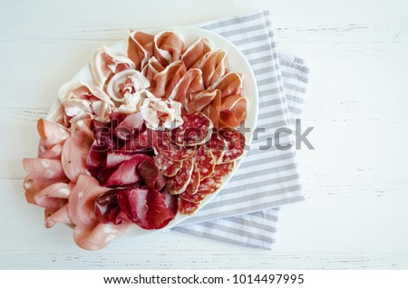 Cold smoked meat plate with pork, prosciutto, salami and bresaola on white wooden background. Wine appetizer set. Italian food. Top view.