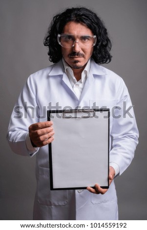 Studio shot of handsome man doctor with mustache wearing protective glasses against gray background