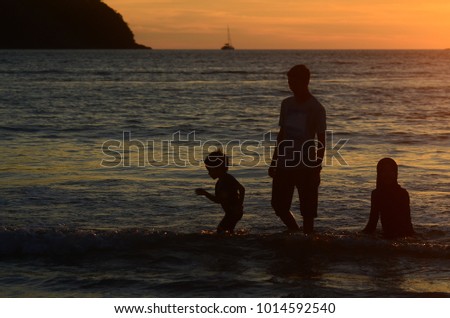 kids and teenagers silhouettes on beach at sunset
