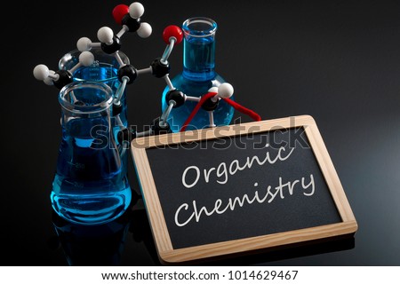 Chemical reaction, science class and STEM concept with a model of a molecule on chemistry glassware and flasks filled with blue liquid and a chalkboard with organic chemistry written on Royalty-Free Stock Photo #1014629467
