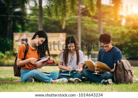 A group of young or teen Asian student in university smiling and reading the book and look at the tablet or laptop computer in summer holiday. Royalty-Free Stock Photo #1014643234