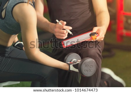 Fitness and healthy concept. Sporty woman workout with dumbbell with trainer checking in gym. Picture for add text message. Backdrop for design art work.