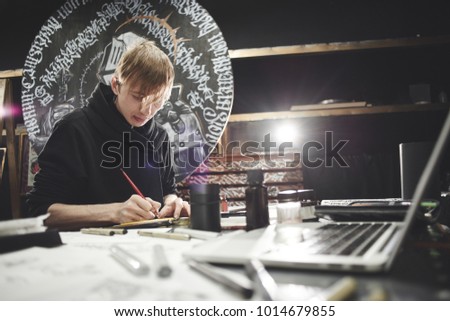 Portrait of a master calligrapher. A tattoo artist makes a sketch while sitting at a table in the Studio