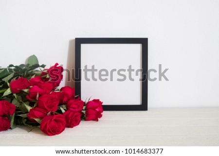 Black square frame photo with red roses bouquet on table